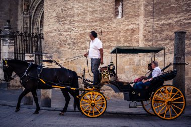 Seville, İspanya, 21 Eylül 2025. Atlı turistler Sevilla şehir merkezinin tarihi bölgesini ziyaret ediyor ve dar, pitoresk caddelerde yürüyor..