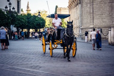 Seville, İspanya, 21 Eylül 2025. Atlı turistler Sevilla şehir merkezinin tarihi bölgesini ziyaret ediyor ve dar, pitoresk caddelerde yürüyor..