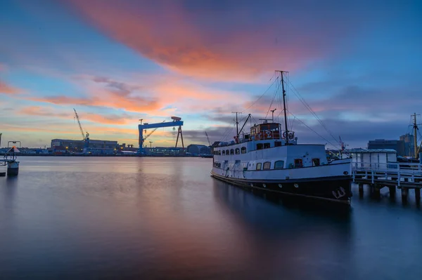 A saloon motor ship stowed at the pier with shipyard area with gantry crane on the background, Kiel, Schleswig-Holstein, Germany. Kiel harbor inner fjord by sunrise.