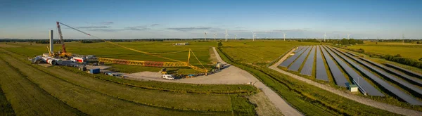 Panoramic view of the construction site of a modern wind turbine in the start-up phase in the background with solar park. The generation of renewable energies combines photovoltaics and wind power.