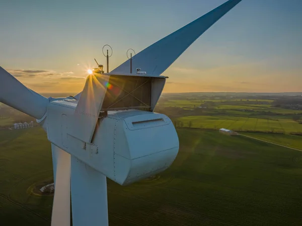 Nacelle of a wind turbine with fields in the backgroundagainst the sun. Aerial view of countryside with a close-up of a wind turbine as seen from the nacelle (hub) against the sun.