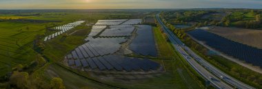 Otoyol boyunca açık alanlarda fotovoltaik manzarası. Güneş enerjisi tesisi, temiz elektrik ve yenilenebilir enerji üretmek için kullanılan büyük bir yolun yanında yer almaktadır..