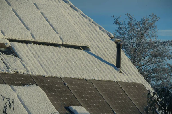 Solar power plant on a roof of residential house covered with snow and ice. Photovoltaic panels on the roof of house covered with snow and ice. Ice accumulation on solar cells. Iced-over solar modules