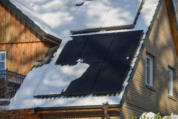 Solar water heater and solar power plant on a roof of residential house covered with snow. Solar thermal collector and photovoltaic panels on the roof of house covered with snow.