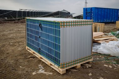 Bir fotovoltaik parkın inşaat alanında güneş modülleri ve güneş panelleri için bileşenler içeren paletler. Arka planda kurulum ve inşaat atığı için paletlerin üzerine istiflenmiş güneş panelleri.