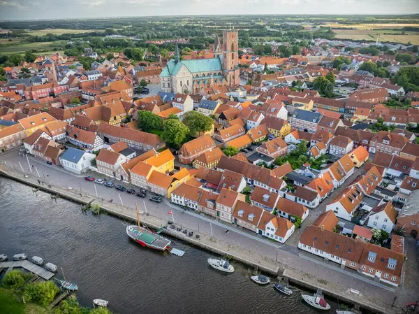 stock image Aerial view of historic town Ribe with majestic Ribe cathedral, red-roofed buildings and boats docked along the riverside, set against lush, green landscape, south-west Jutland, Denmark.