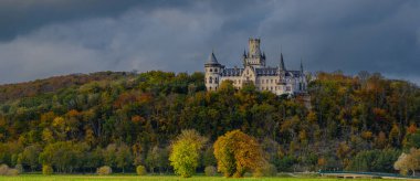 Panoramic view of Marienburg Castle, historic Gothic Revival masterpiece in Lower Saxony, Germany, rising atop a hill, with ornate towers and intricate architecture framed by autumn foliage. clipart