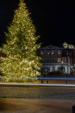 Christmas tree adorned with sparkling lights and light trails stands gracefully, with half-timbered houses on the Paradeplatz in Rendsburg serving as a charming backdrop. clipart