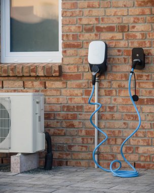 Close-up of modern brick house wall with an electric vehicle charging station with blue cable and air conditioning. Modern home with energy-efficient solutions electric vehicle (EV) charging station. clipart