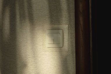 Yumuşak güneş ışığıyla aydınlatılan dokulu bir duvardaki ışık düğmesi. Gölgeler sakin ve rahat bir atmosfer yaratıyor. Minimalist ev iç dekorasyonu