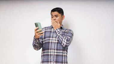 Beyaz arka planda cep telefonu kullanan Asyalı genç adam şok olmuş yüz ifadesi sergiliyor