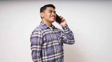 Asyalı genç adam akıllı telefonda konuşurken gülen yüz ifadesi gösteriyor. Beyaz arkaplan karşısında stüdyo görüntüleri