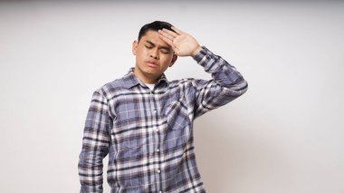Mutsuz, hasta, genç Asyalı bir adam şiddetli baş ağrısından muzdarip. Alnına kapalı gözlerle dokunuyor. Stüdyo fotoğrafı, soğuk algınlığı, grip, koronavirüs, grip, fotokopi odası.