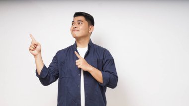 Genç Asyalı adam beyaz arka planda sağ tarafa bakıp işaret ederken gülümsüyor. Stüdyo çekimi