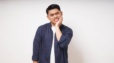 Diş ağrısı konsepti. Asyalı bir adam beyaz arka planda acı ifadesiyle çenesine dokunuyor. Stüdyo çekimi