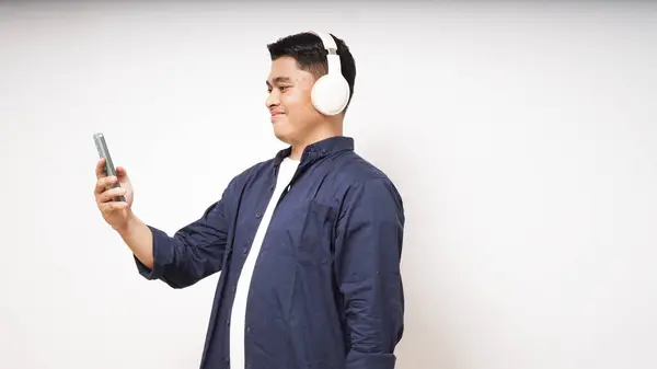 stock image Happy young Asian man wearing wireless headphones listening to music from smartphone studio shot isolated on white background