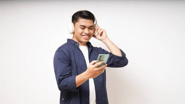 Beyaz arka planda izole edilmiş akıllı telefon stüdyosundan müzik dinleyen, kablosuz kulaklık takan mutlu Asyalı genç adam.