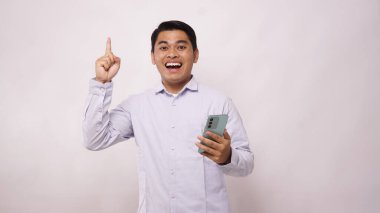 Asyalı bir adam beyaz arka planda telefonuna bakarken heyecanını gösteriyor.