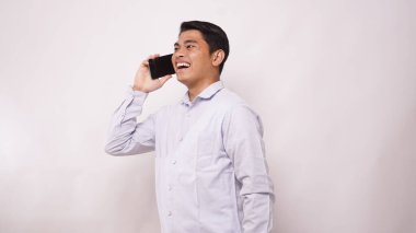 Beyaz arka plandaki bir cep telefonuna cevap verirken kameraya gülümseyen Asyalı bir adam