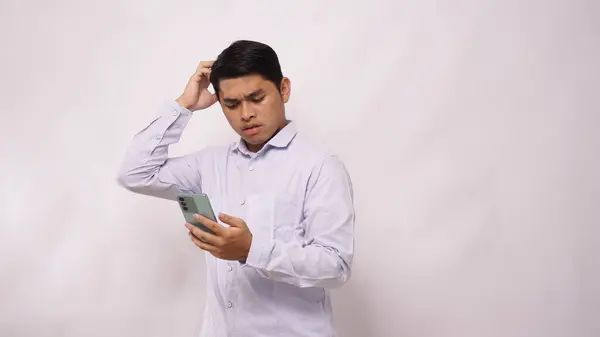 Asian man scratch his head while holding mobile phone and showing confused face expression against white background