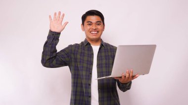 Asyalı öğrenci dizüstü bilgisayarını beyaz arka planda tutarken el sallıyor