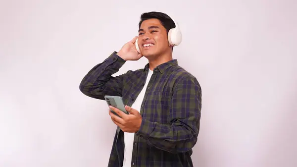 Asian young man listening music on smartphone using headphone wireless against white background