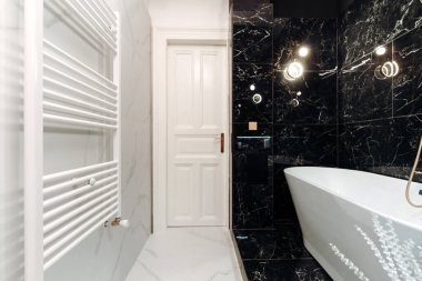 Details of fancy bathroom with modern appliances and LED fixtures, freestanding tub with black and white marble