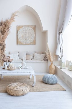 daylight through a huge panoramic window illuminates the cozy oriental interior of the room in beige colors with wicker furniture and authentic elements