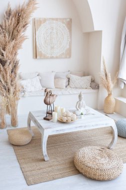 daylight through a huge panoramic window illuminates the cozy oriental interior of the room in beige colors with wicker furniture and authentic elements