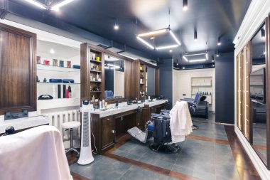 Lüks berber dükkanı, mavi pahalı mobilyalar, ahşap süslemeler, moda siyah tavan, koltukların arkasında beyaz bornozlar.