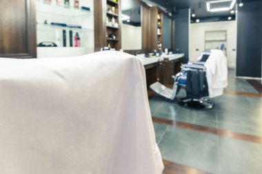 Lüks berber dükkanı, mavi pahalı mobilyalar, ahşap süslemeler, moda siyah tavan, koltukların arkasında beyaz bornozlar.