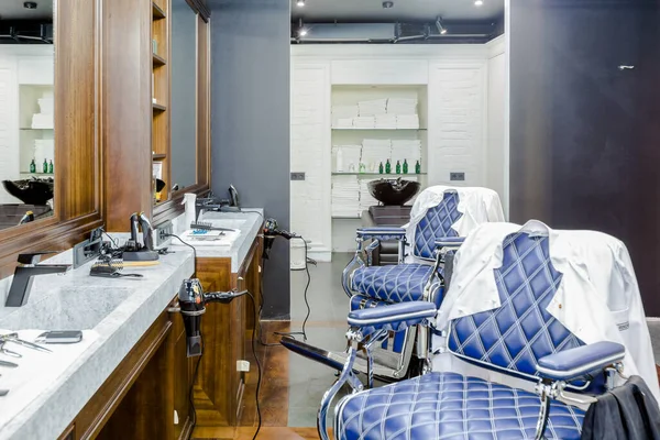 stock image luxury barber shop interior, blue expensive furniture, wood trim, fashionable black ceiling, white robes on the backs of armchairs