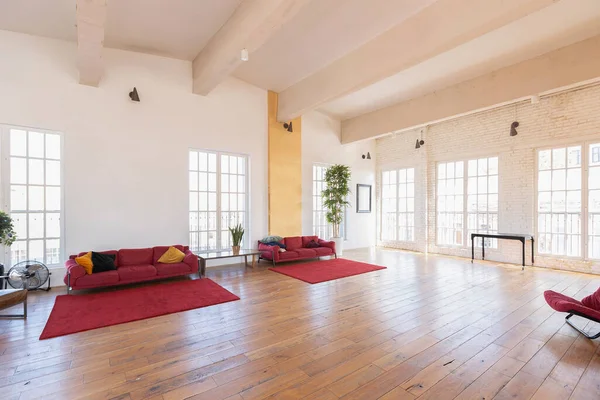 现代设计的一个巨大的白色明亮的房间 有两个红色沙发和许多大窗户 充满了阳光 高高的天花板和木制花篮 — 图库照片