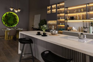 Son derece modern, koyu renkli, süper havalı ışıklandırmalı, yemek pişirmek için bir ada ve yemek masası olan bir dairede lüks bir mutfak.