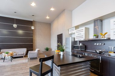 Yumuşak ve sıcak renklerde çağdaş, sıradan bir stüdyo tasarımı. Basit mobilyalar. Güneş ışığıyla aydınlık geniş bir oda. Gündüz vakti. Döşeme kahverengi zemin ve beyaz duvarlar .