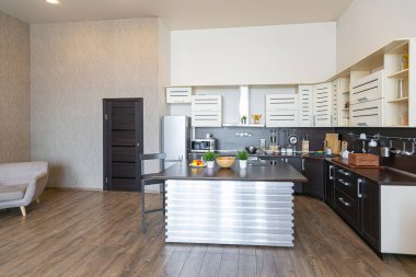 Yumuşak ve sıcak renklerde çağdaş, sıradan bir stüdyo tasarımı. Basit mobilyalar. Güneş ışığıyla aydınlık geniş bir oda. Gündüz vakti. Döşeme kahverengi zemin ve beyaz duvarlar .