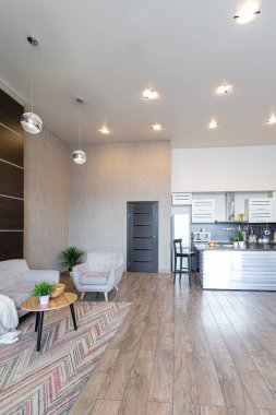 Yumuşak ve sıcak renklerde çağdaş, sıradan bir stüdyo tasarımı. Basit mobilyalar. Güneş ışığıyla aydınlık geniş bir oda. Gündüz vakti. Döşeme kahverengi zemin ve beyaz duvarlar .