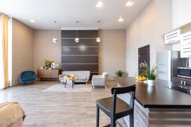 Yumuşak ve sıcak renklerde çağdaş, sıradan bir stüdyo tasarımı. Basit mobilyalar. Güneş ışığıyla aydınlık geniş bir oda. Gündüz vakti. Döşeme kahverengi zemin ve beyaz duvarlar .