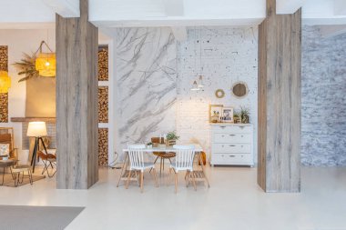 Tavan arasında ahşap sütunlar olan, tuğla, mermer, ahşap, şık mobilyalar ve beyaz duvarlarla süslenmiş, aydınlık bir stüdyo dairesinin modern iç mimarisi.