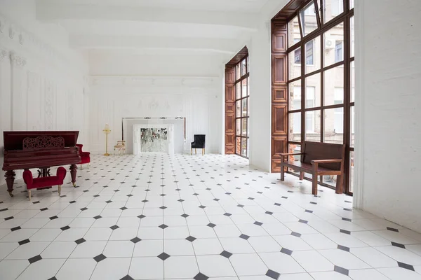 stock image Huge luxury white hall with unique interior. Black and white tiles on the floor, white and black stucco on the walls, high fireplace with mirror mosaic, three-meter crystal chandelier and grand piano