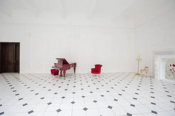 stock image Huge luxury white hall with unique interior. Black and white tiles on the floor, white and black stucco on the walls, high fireplace with mirror mosaic, three-meter crystal chandelier and grand piano