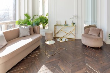 Şık, yumuşak bej mobilyalı, altın metalik elementli, yere açılan kocaman pencereli ve ahşap parke kaplı lüks ve parlak bir oturma odası.