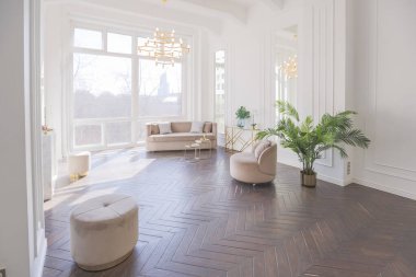 Şık, yumuşak bej mobilyalı, altın metalik elementli, yere açılan kocaman pencereli ve ahşap parke kaplı lüks ve parlak bir oturma odası.