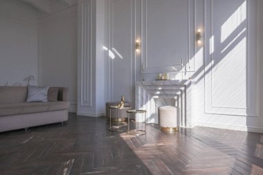 Şık, yumuşak bej mobilyalı, altın metalik elementli, yere açılan kocaman pencereli ve ahşap parke kaplı lüks ve parlak bir oturma odası.