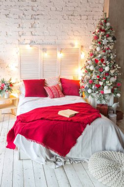 Süslü Noel ağacı ve çelengi olan, tavan arası tarzı geniş, beyaz bir yatak odası..