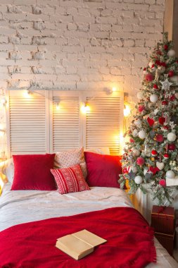Süslü Noel ağacı ve çelengi olan, tavan arası tarzı geniş, beyaz bir yatak odası..