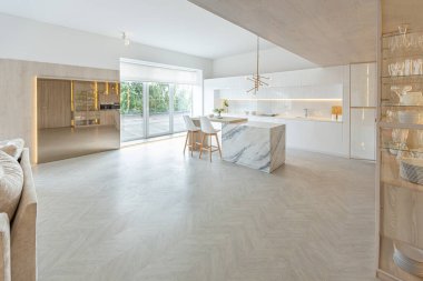 Modern moda kar beyazı mutfağının lüks iç tasarımı. Minimalist tarzda, ada ve iki bar taburesi. Yere kocaman pencereler ve bulaşıklar için cam askı.