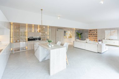 Beyaz ve bej renkli geniş tabandan tavana kadar pencereleri olan büyük bir stüdyonun modern iç tasarımı. Adayı ve dinlenme alanı olan beyaz mutfak.