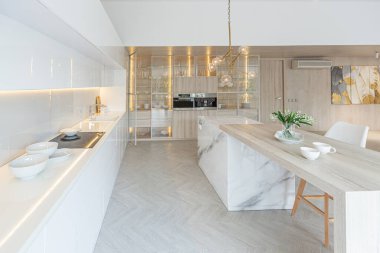 Modern moda kar beyazı mutfağının lüks iç tasarımı. Minimalist tarzda, ada ve iki bar taburesi. Yere kocaman pencereler ve bulaşıklar için cam askı.