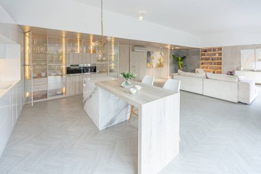 Modern moda kar beyazı mutfağının lüks iç tasarımı. Minimalist tarzda, ada ve iki bar taburesi. Yere kocaman pencereler ve bulaşıklar için cam askı.